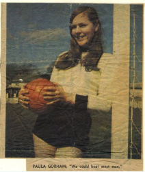 Smiling woman in football kit holding a football and leaning on a goalpost